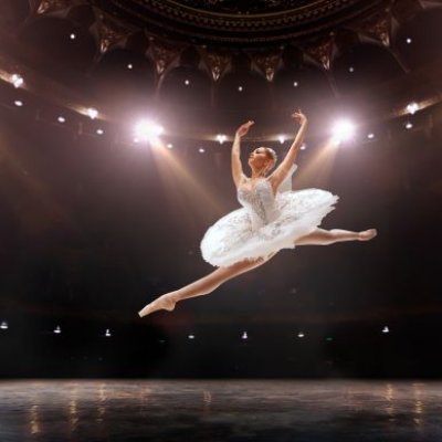 A ballet dancer in white tutu leaping under lights on stage. Adobe